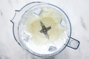 feta, a garlic clove, yogurt, water and olive oil in being blended together in a blender