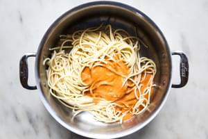 cooked bucatini noodles being tossed with spicy roasted red paper sauce in a stock pot