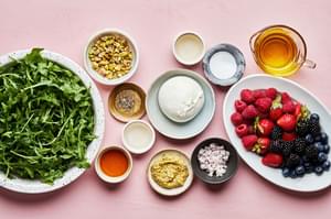 arugula, mixed berries, burrata pistachios and ingredients for homemade balsamic vinaigrette in bowls on the counter