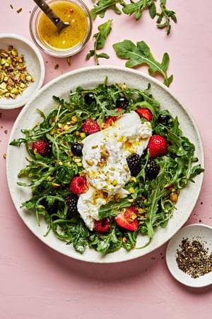 Burrata Salad with Summer Berries & Pistachios surrounded by bowls of pistachios, dressing and fresh cracked pepper
