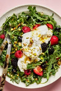 Burrata Salad with Summer Berries & Pistachios tossed with homemade balsamic vinaigrette in a serving bowl with salad servers