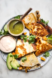 butternut squash quesadilla with caramelized onions on a plate served with avocado, salsa verde, chipotle cream & cilantro