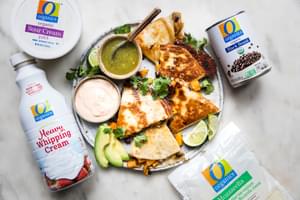 a butternut squash quesadilla on a plate surrounded by organics brand mozzarella, sour cream, black beans & heavy cream