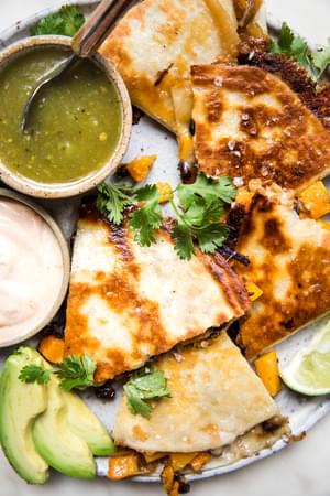 butternut squash quesadilla with caramelized onions on a plate served with avocado, salsa verde, chipotle cream & cilantro