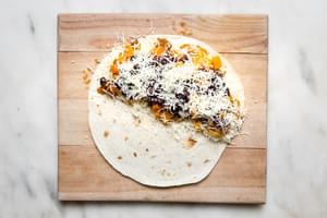 a flour tortilla with mozzarella, caramelized onions, roasted butternut squash & black beans on half of it