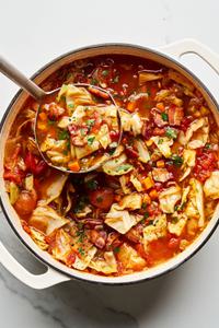 A large pot of homemade cabbage soup topped with fresh chopped parsley with a ladle scooping out a a serving