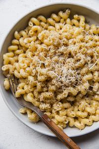homemade Creamy Cavatappi in a bowl with a fork topped with grated Romano and coarsely cracked pepper