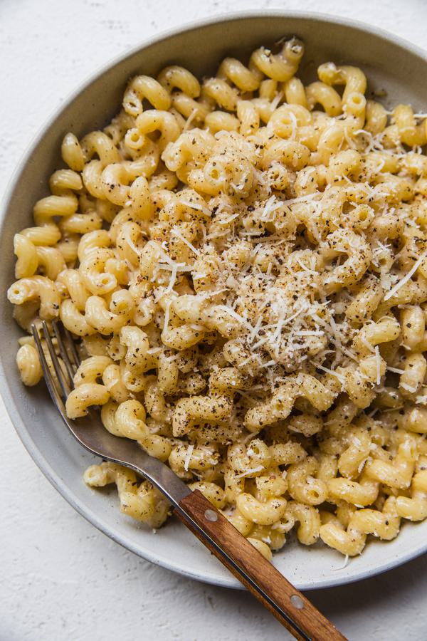 homemade Creamy Cavatappi in a bowl with a fork topped with grated Romano and coarsely cracked pepper