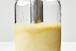 homemade caesar dressing being blended together in a glass jar with an immersion blender
