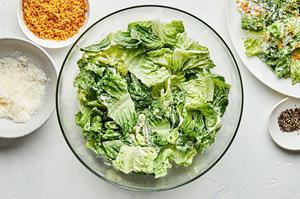 Caesar salad with homemade caesar dressing in a bowl beside bowls of parmesan, toasted breadcrumbs and pepper for topping
