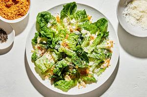 homemade Caesar salad with homemade caesar dressing, surrounded by bowls of toasted breadcrumbs, pepper and Parmesan