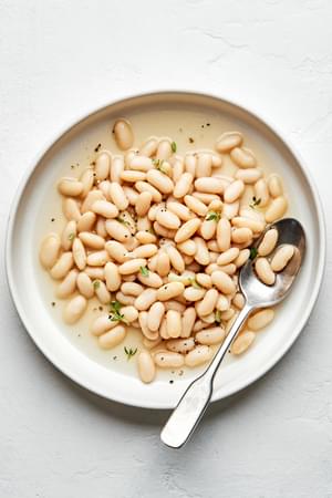 homemade cannellini beans made with onion, bay leaves, thyme, garlic, salt & pepper in a bowl with a spoon