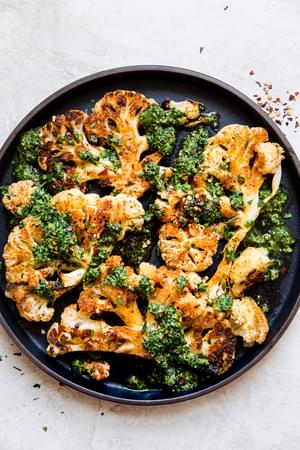 black plate of cauliflower steaks topped with a walnut kale pesto