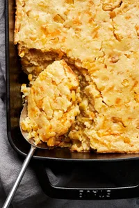 cheesy corn casserole made with corn and creamed corn in a casserole dish with a spoon scooping out a serving