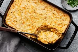 cheesy corn casserole made with corn and creamed corn in a casserole dish with a spoon scooping out a serving