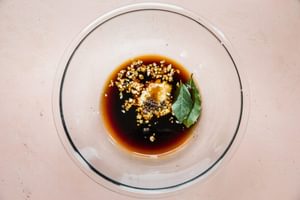 chicken adobo marinade made with vinegar, soy sauce, garlic, peppercorns, bay leaves and brown sugar in a glass bowl