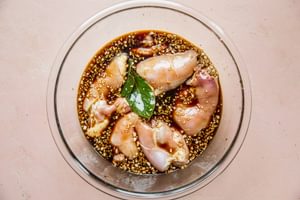 A glass bowl filled with boneless, skinless, chicken thighs being marinated in adobo sauce