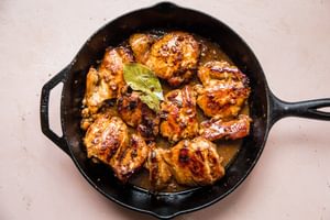 Chicken adobo simmering in a skillet, with pieces of chicken coated in a rich, dark sauce