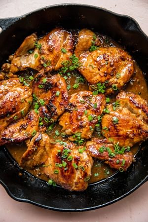 Chicken adobo simmering in a skillet, with pieces of chicken coated in a rich, dark sauce sprinkled with green onions