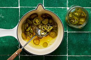 sliced jalapeños, sugar, lemon zest, water and apple cider vinegar being stirred in a pot to make candied jalapeños