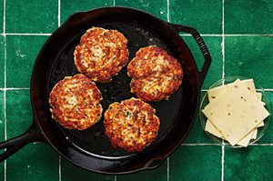 homemade chick burger patties being fried in a skillet with pepper jack cheese slices on the counter beside it