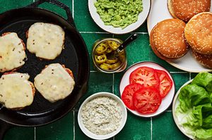 chicken patties with pepper jack in a skillet next to all the fixing include basil mayo, avocado spread and candied jalapeños