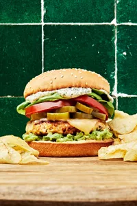 chicken burger with basil mayo, avocado spread, candied jalapeños, pepper jack cheese, lettuce and tomato on a cutting board