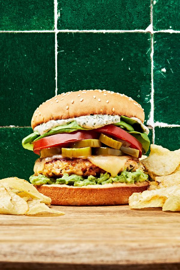 chicken burger with basil mayo, avocado spread, candied jalapeños, pepper jack cheese, lettuce and tomato on a cutting board