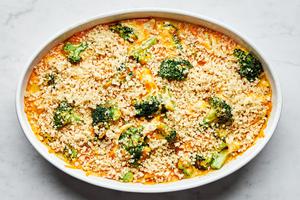 chicken divan in a casserole dish topped with shredded cheese and panko breadcrumbs ready to be baked