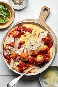 homemade chicken meatballs with polenta topped with shaved parmesan and marinara in a bowl with a spoon
