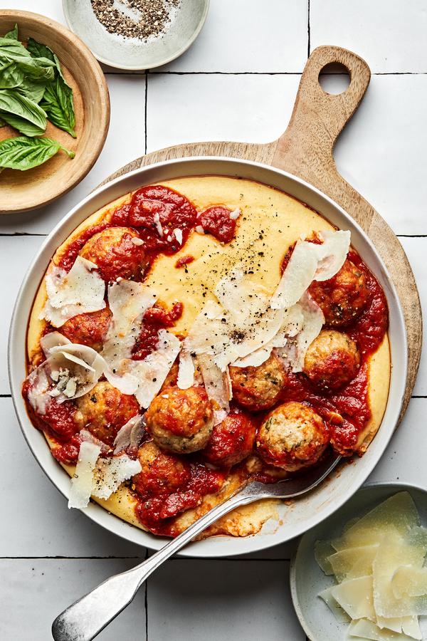 homemade chicken meatballs with polenta topped with shaved parmesan and marinara in a bowl with a spoon