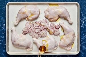 chicken quarters patted dry, seasoned with salt and sliced shallots on a baking sheet ready for the oven