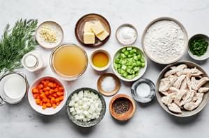 A variety of ingredients for chicken and dumplings in prep bowls: chicken, vegetables, broth, flour, butter, and seasonings