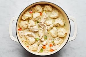 A pot of chicken and dumplings with homemade dumplings with vegetables in a creamy broth