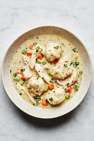 A bowl of chicken and dumplings with homemade dumplings in a creamy broth, garnished with herbs