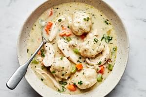 A bowl of chicken and dumplings with homemade dumplings in a creamy broth, garnished with herbs