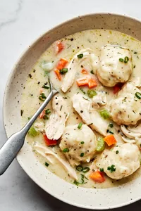 A bowl of chicken and dumplings with homemade dumplings in a creamy broth, garnished with herbs