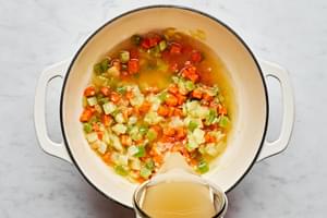 stock being added to a pot with onion, carrots, celery, garlic, olive oil, butter and flour to make chicken and dumplings