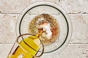 olive oil being poured into a bowl with garlic powder, oregano, basil, salt, vinegar and sugar to make Italian dressing