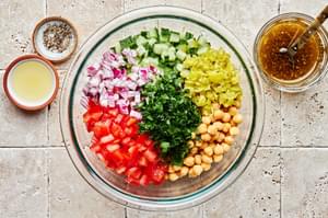 chickpea salad with cucumber and tomatoes in a bowl beside bowls of Italian dressing, lemon juice, salt & pepper