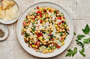 Homemade chickpea salad with Italian dressing, sprinkled with parmesan cheese in a serving bowl beside extra parmesan