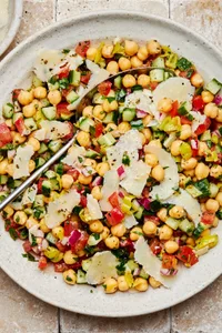 Chickpea salad tossed with homemade Italian dressing and sprinkled with parmesan cheese in a bowl with a serving spoon.