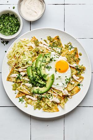 chilaquiles on a plate made with homemade tortilla chips topped with cabbage, salsa verde, crema, avocado and a fried egg