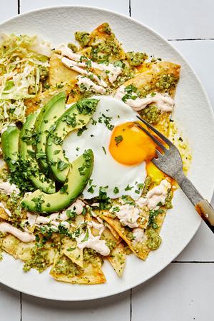 chilaquiles on a plate made with homemade tortilla chips topped with cabbage, salsa verde, crema, avocado and a fried egg