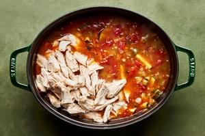 rotisserie chicken being added to a pot of homemade chipotle chicken soup made with corn, black beans & chipotle chilis