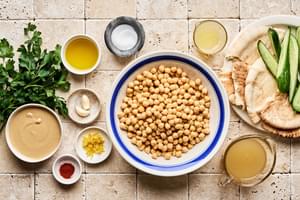 Chickpeas, tahini, olive oil, lemon juice, garlic, salt, cucumber, pita, parsley, paprika, & za'atar laid out to make hummus