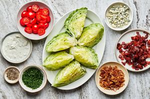 a platter with wedges of iceberg lettuce surrounded by bowls of bacon, fried shallots, blue cheese dressing & tomatoes