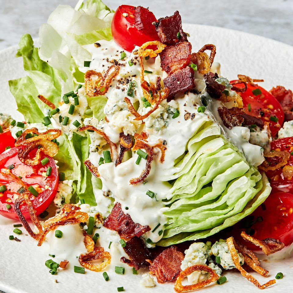 a classic wedge salad topped with homemade blue cheese dressing, blue cheese, bacon, cherry tomatoes and fried shallots
