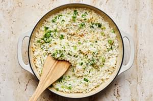 coconut rice, green onions, coconut flakes and ginger being cooked in coconut oil in a pan with a wooden spoon
