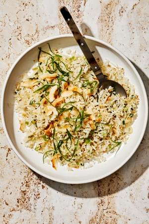 homemade coconut fried rice with green onions, ginger, and sweetened coconut flakes in a serving bowl with a wooden spoon